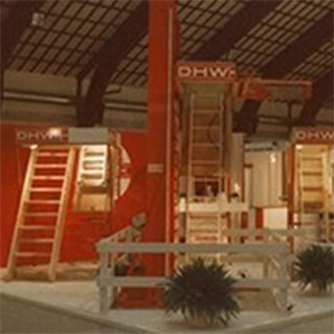 Foto do estande de exposição da Dolle em 1984, com escadas vermelhas e uma apresentação de produtos em um ambiente de salão profissional.