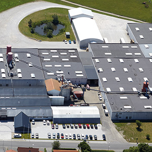Vista aérea da sede da Dolle na Dinamarca, mostrando um grande estabelecimento com estacionamento e vegetação ao redor.