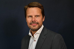 Retrato de Laurent Schmidt, CEO da SOGEM, usando um terno escuro e uma camisa branca sobre fundo preto.