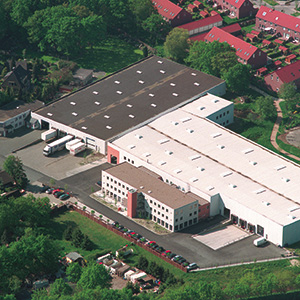 Vista aérea da fábrica da Dolle em Bremen, mostrando um grande edifício rodeado por vegetação.