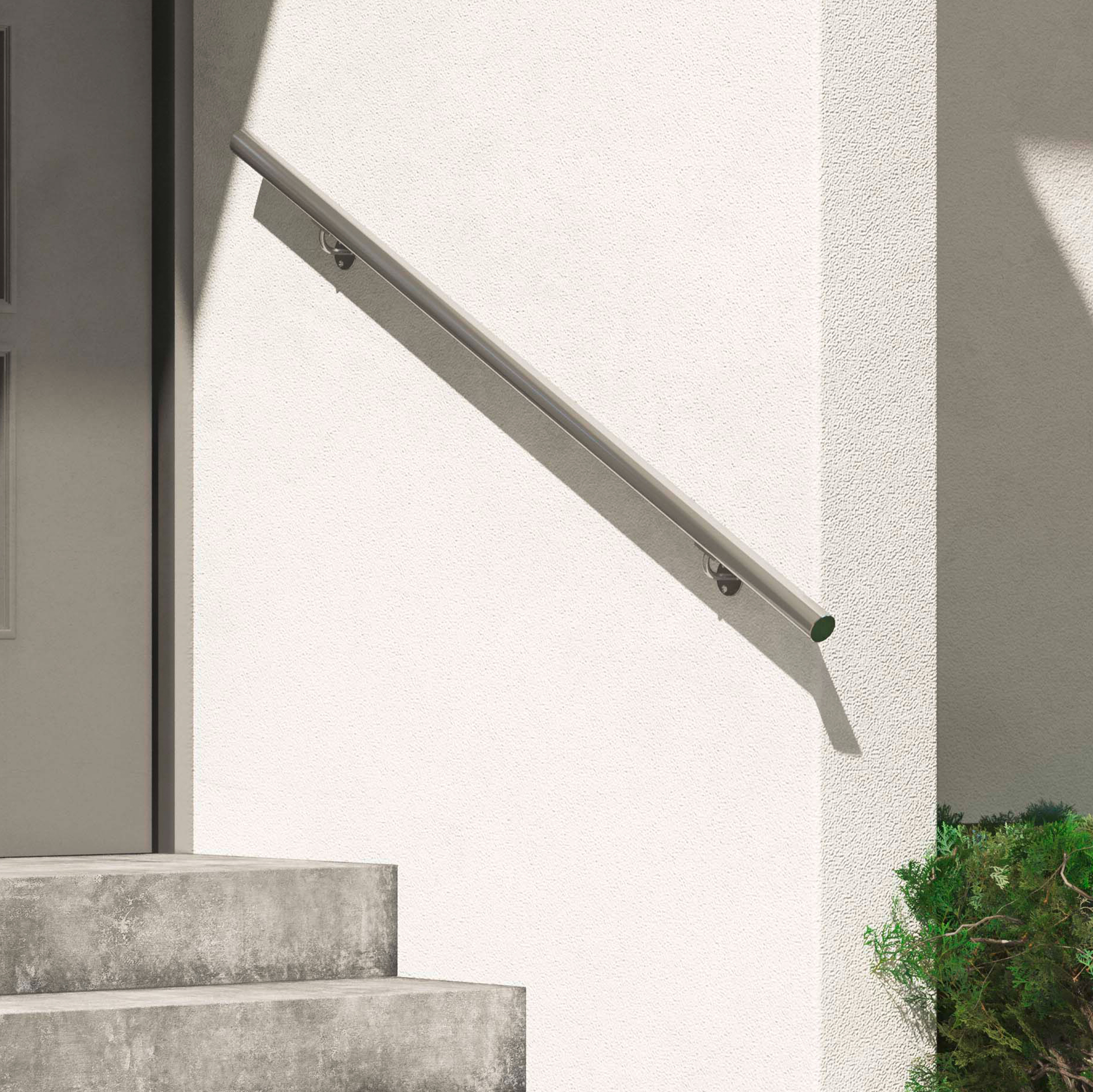 Corrimão metálico minimalista em uma parede externa branca, ao lado de degraus de concreto e vegetação.